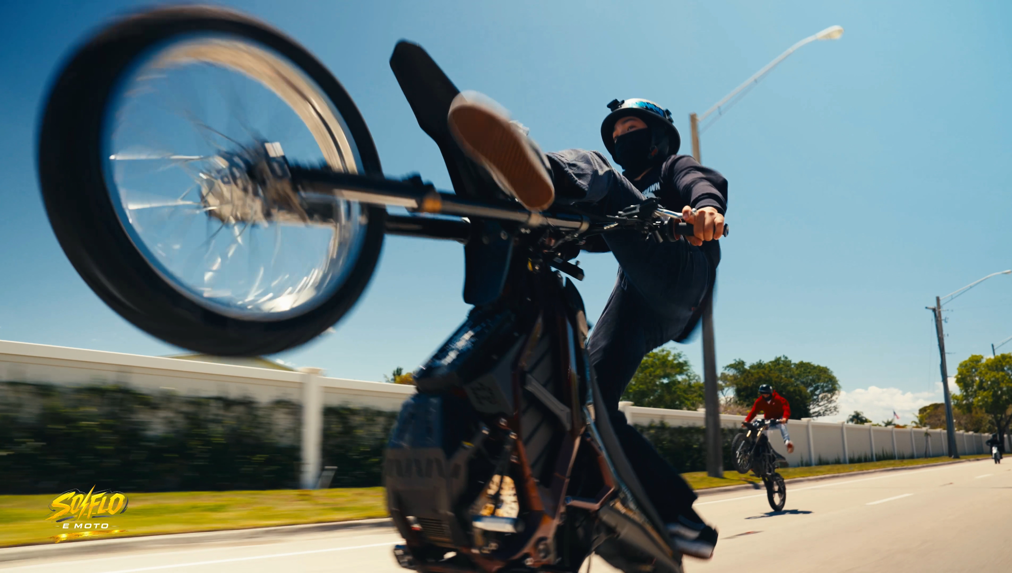 SoFlo E-Moto rider doing a wheelie on a palm-lined South Florida road