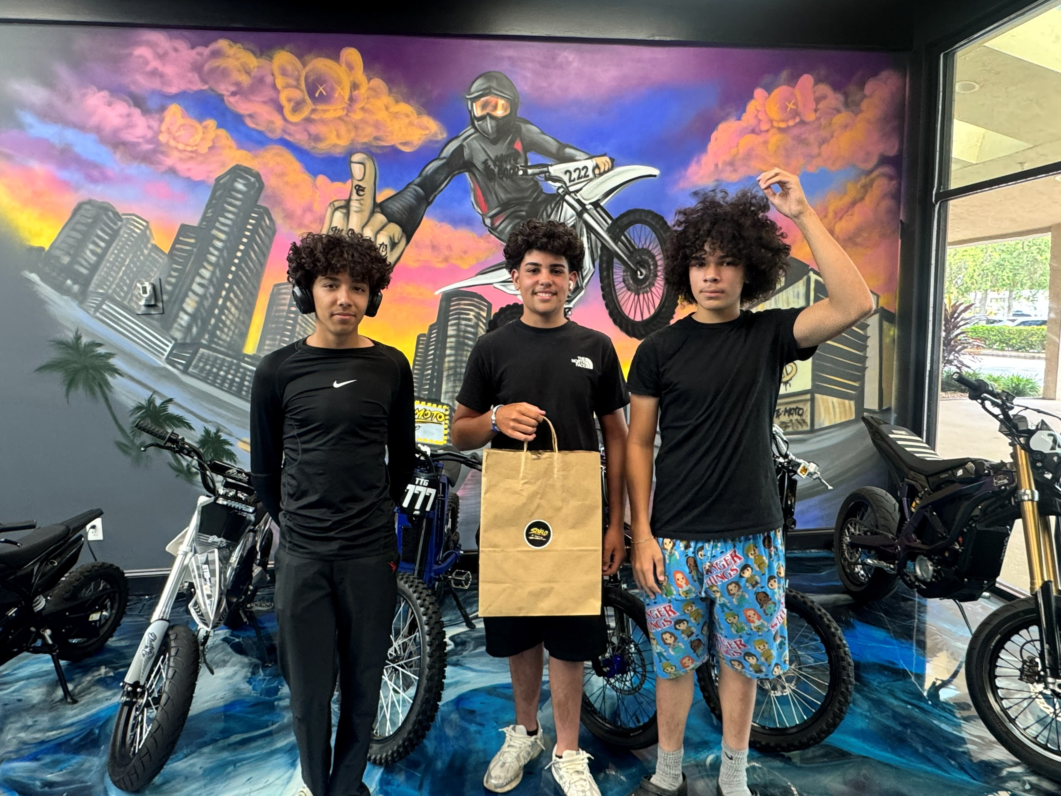 SoFlo E-Moto crew standing with bikes in front of the mural wall inside the shop