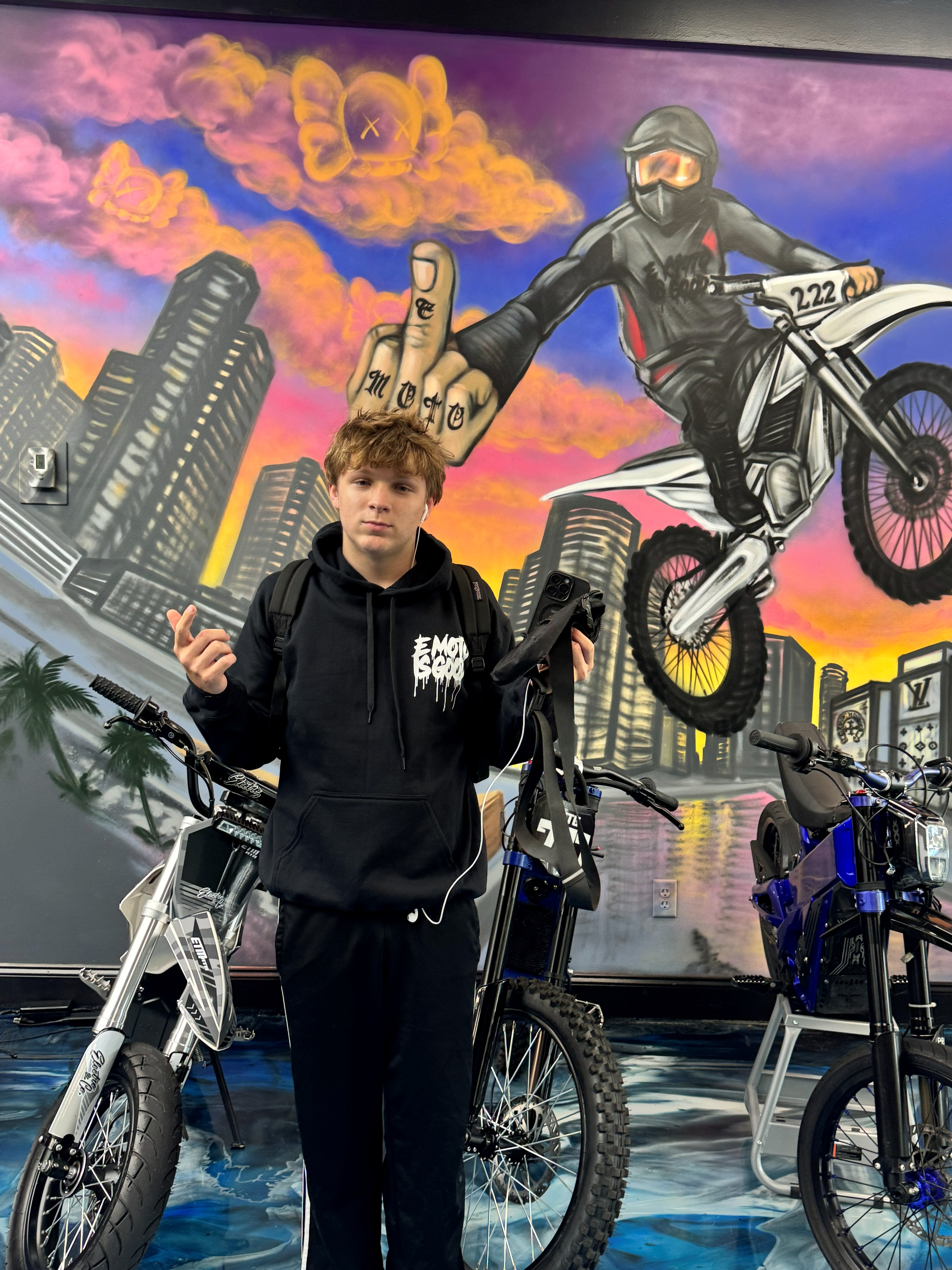 SoFlo E-Moto crew member standing between e-bikes in front of the mural wall